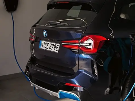 BMW iX3 Elektroauto in der Farbe Blau Ansicht von hinten beim Laden an einer Wallbox