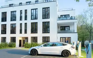 E-Auto lädt an einer Ladestation vor Mehrfamilienhaus: Förderung 2026 ist geplant