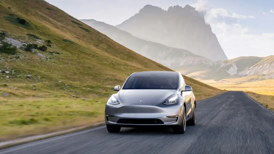 Tesla Model Y fährt auf einer Straße in einer leicht bergigen Landschaft.