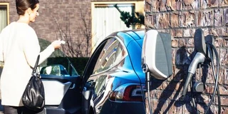 EVBox Elvi Wallbox an Backsteinwand im Hintergrund Frau vor E-Auto