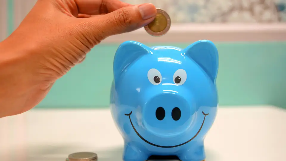 Hand schmeißt Geld in ein lachendes blaues Sparschwein
