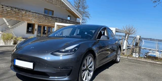 Tesla Model 3 Grau vor Haus am See beim Laden