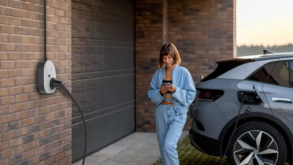 Eine Frau steht vor der Garage und aktiviert ihre go-e Wallbox für das Überschussladen