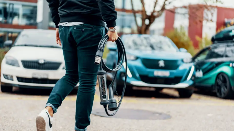 Person trägt Juice Booster 3 air zum E-Auto – beste mobile Wallbox für unterwegs
