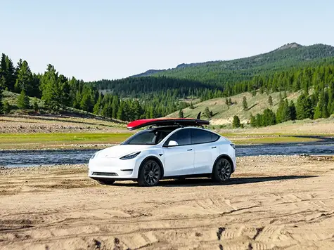 Tesla Model Y in Farbe weiß mit Surfbrett auf dem Dach