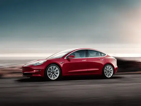 Tesla Model 3 Elektroauto in der Farbe rot Ansicht von schräg Vorne während der Fahrt